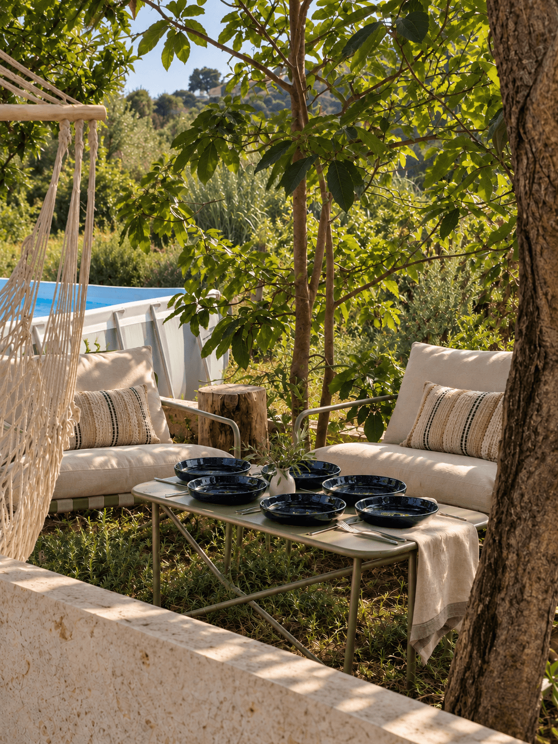 Cushioned garden seating and a low table beneath the trees beside the pool.