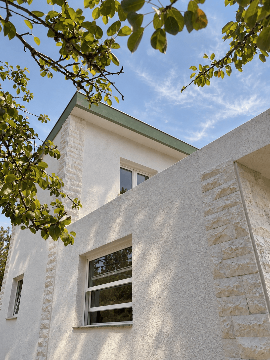 White house exterior with pale green trim framed by leaves.